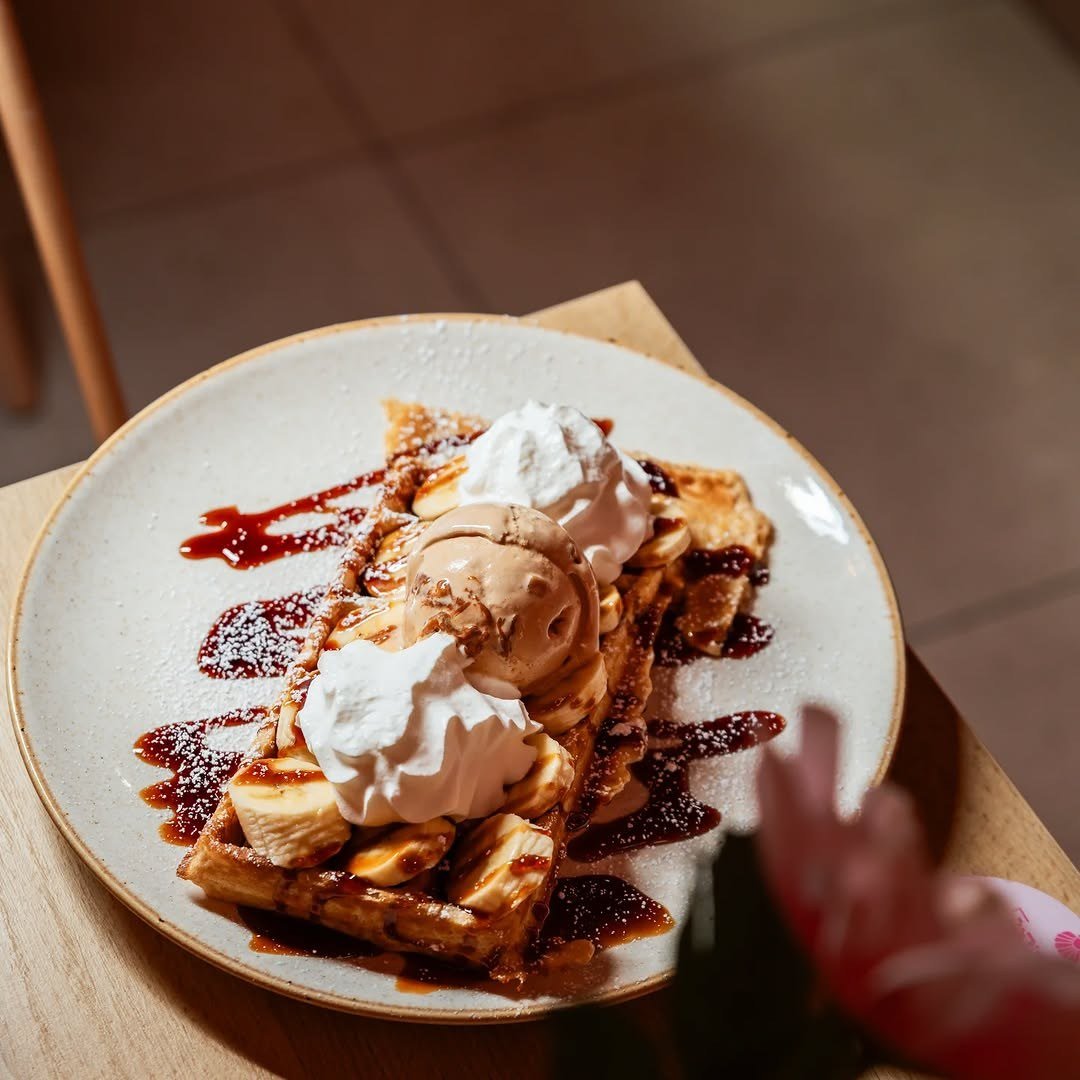 Waffle com gelado, natas e caramelo num prato de bordo castanho