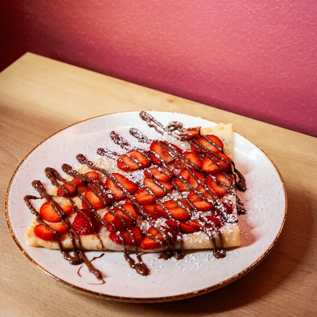 Crepe dobrado com morangos laminados e fios de chocolate num prato